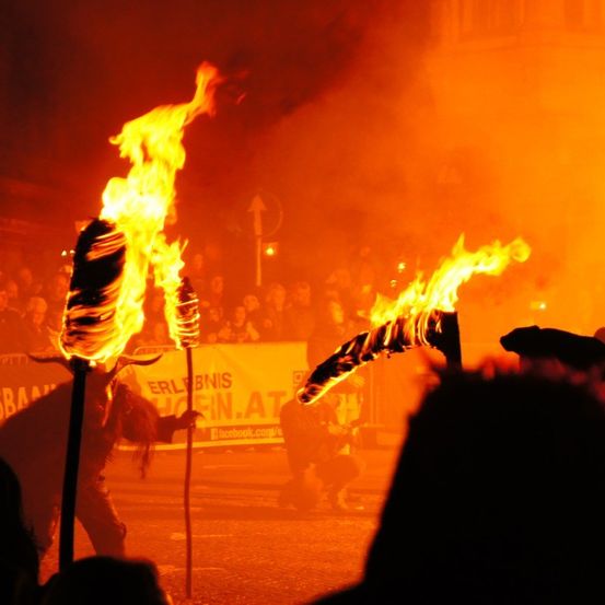 Eine Person hält eine flammende Fackel und führt eine Aufführung vor einem Publikum bei einer Veranstaltung im Freien durch.