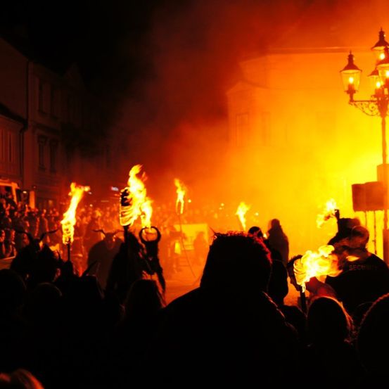 Ein nächtliches Festival mit Feuerfackeln und Zuschauern, vor dem Hintergrund von Gebäuden und einer Straßenlaterne.