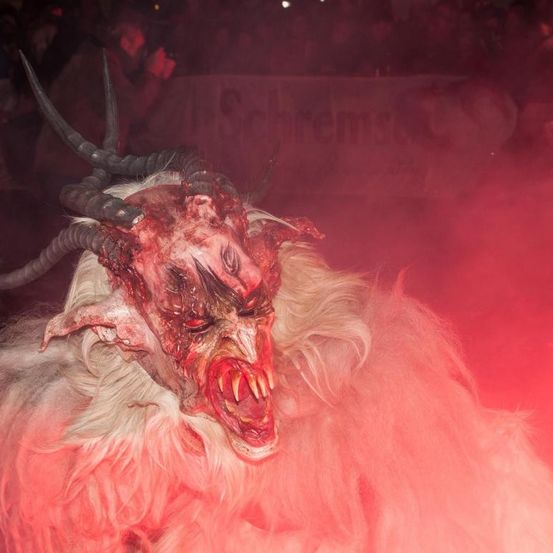 Eine Person in einem Hornmaskenkostüm mit roter Beleuchtung ist auf einem Festival. Der Hintergrund ist verschwommen mit Menschen.