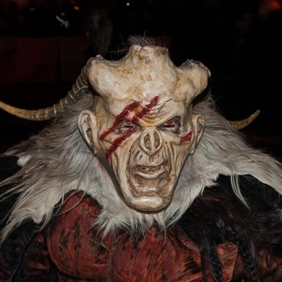 Eine Nahaufnahme einer Halloween-Maske, die einen gehörnten Dämon darstellt, mit Blutspuren im Gesicht und weißem Fell am Hals.