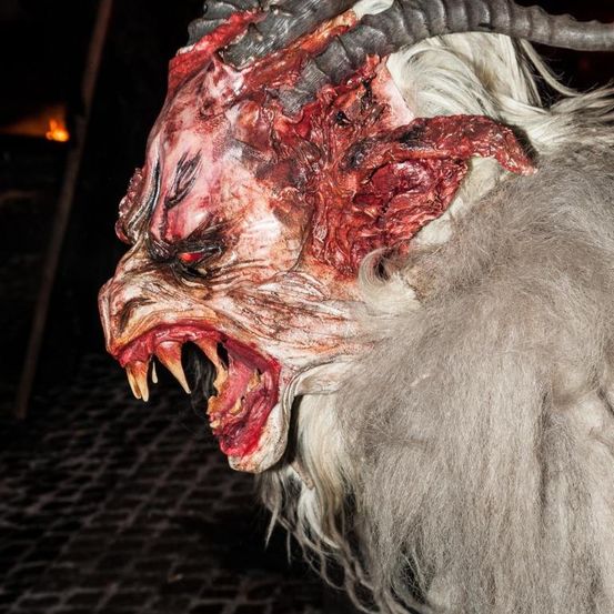 Nahaufnahme eines wolfsartigen Wesens mit Blut im Gesicht, das seine Reißzähne und einen bedrohlichen Ausdruck zeigt.