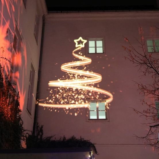 Eine spiralförmige Weihnachtsbaum-Lichtprojektion an einem Gebäude bei Nacht, mit Funkeleffekten und einem Stern oben.