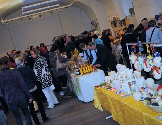 Eine Menschenmenge in einem Raum mit Tischen und dekorativen Gegenständen, eine Person betrachtet eine gelbe Kerze.