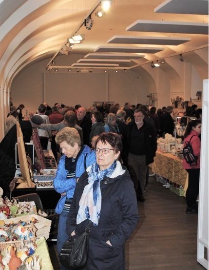 Ein überfüllter Indoor-Markt mit Menschen, die verschiedene Artikel auf Displaytischen betrachten, unter Deckenbeleuchtung.