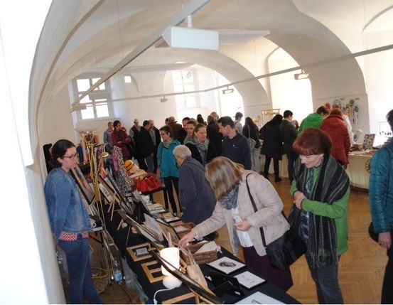 Eine Menschenmenge betrachtet Gegenstände auf einem Indoor-Markt in einem Raum mit hohen Decken, Holzböden und großen Fenstern.