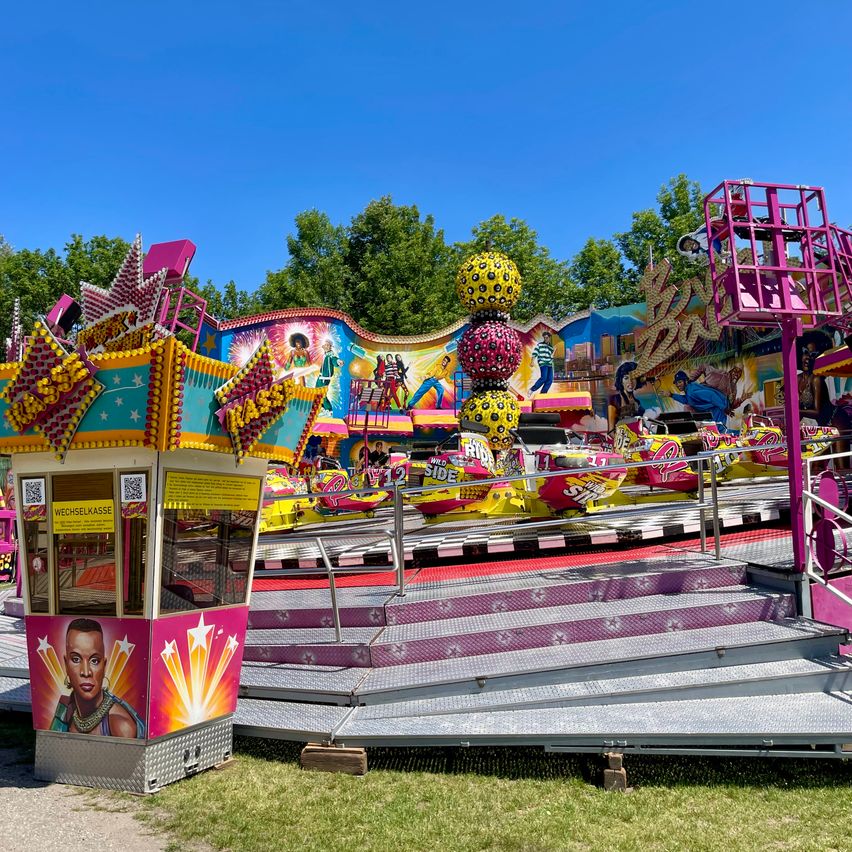 Eine bunte Achterbahn im Vergnügungspark mit verschiedenen Autos auf der Strecke, umgeben von grünem Gras und Bäumen.