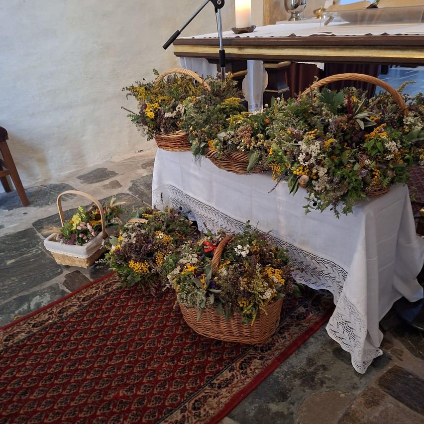 Ein mit einem weißen Tuch bedeckter Tisch hält mehrere Körbe mit verschiedenen Blumen und Kräutern. Die Körbe sind auf einem roten Teppich angeordnet.