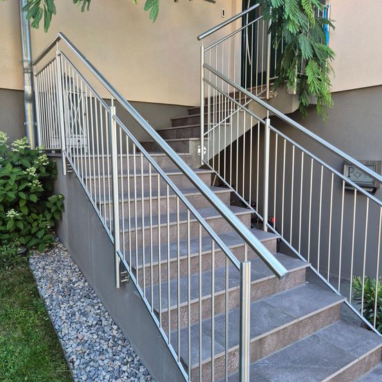 Eine Reihe von grauen Treppen mit Metallgeländern führt zu einem Gebäude mit einer Rohrleitung und Pflanzen an der Seite.