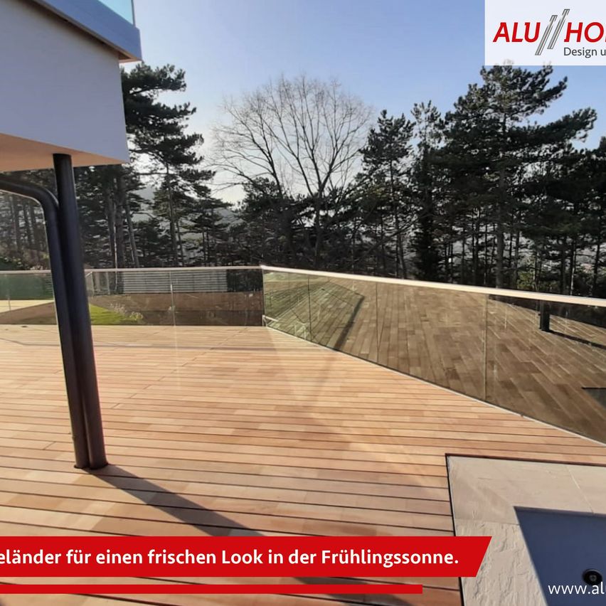 Ein Balkon mit Glasgeländer und Holzboden, der ein modernes Design präsentiert, mit Blick auf üppige Bäume im Hintergrund.