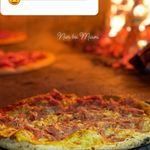 Eine Pizza mit geschmolzenem Käse und Belägen backt in einem Holzofen mit einer hellen Flamme im Hintergrund.