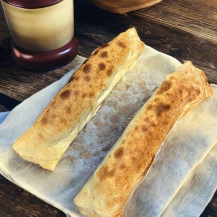 Zwei goldbraune Gebäckstücke mit gesprenkelten Mustern liegen auf einem Pergamentpapier auf einer Holzoberfläche. Links steht ein brauner Kerzenhalter.