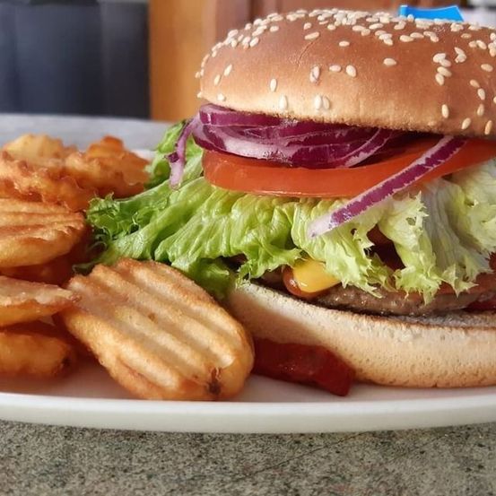 Ein Hamburger mit Salat, Tomate, Zwiebel und Speck liegt auf einem weißen Teller mit Pommes Frites.
