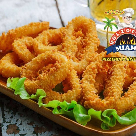 Ein Teller mit knusprigen frittierten Tintenfischringen mit grünem Salat, begleitet von einem Glas Bier und einem Logo für Holzofen Miami Pizzeria & Ristorante.