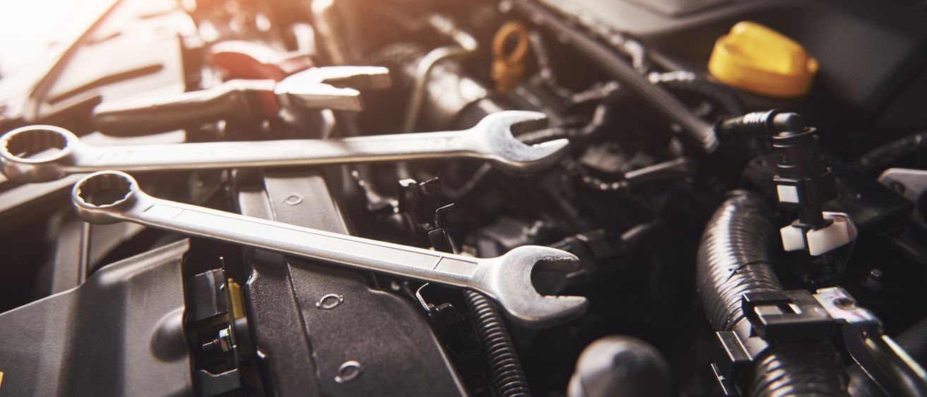 Zwei Schraubenschlüssel ruhen auf einem Automotor, wobei das Sonnenlicht die Szene hervorhebt. Der Motor ist teilweise geöffnet und zeigt mechanische Komponenten.