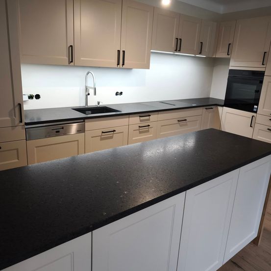 Eine moderne Küche mit weißen Schränken, schwarzen Granitarbeitsplatten und einem Edelstahlspülbecken mit Wasserhahn. Die Küche hat auch einen eingebauten Backofen und Geschirrspüler.