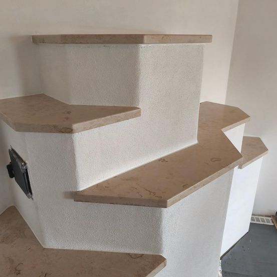 Nahaufnahme einer weißen Wand mit einer Marmortreppe mit drei Stufen. Jede Stufe hat eine beige Marmorstufe und -aufstieg. Die Wand ist glatt und weiß.