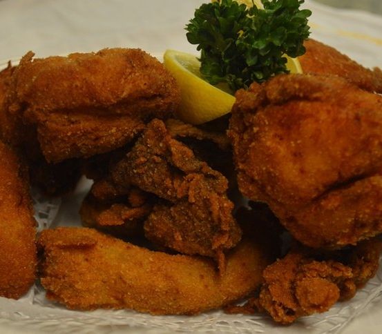 Gebratener Meeresfrüchteteller mit Zitronenspalte und Petersiliengarnitur auf einem weißen Doily.