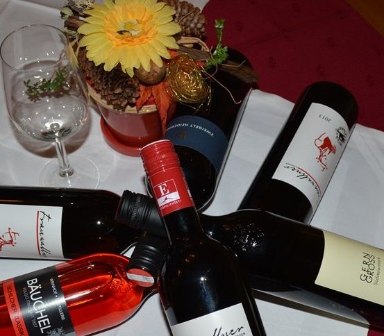 Fünf Weinflaschen und ein Weinglas stehen auf einem Tisch, mit einer roten Tischdecke und einem dekorativen Blumen-Centerpiece.