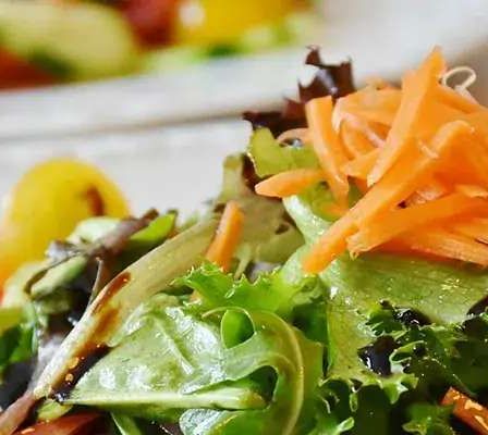 Ein Nahaufnahme eines frischen Salats auf einem weißen Teller mit geriebenen Karotten, Tomaten und grünem Blatt. Der Salat sieht leuchtend und appetitanregend aus und deutet auf eine gesunde Mahlzeit hin.