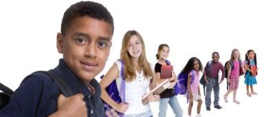 Eine Gruppe von Kindern in Schuluniformen, die in einer Reihe stehen, ein Junge mit Rucksack im Vordergrund.