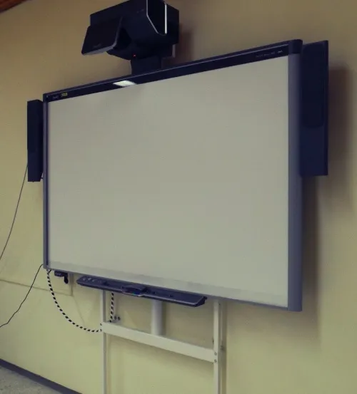 Eine Whiteboard ist an einer Wand montiert, mit einem Lautsprecher oben und zwei zusätzlichen Lautsprechern an den Seiten.