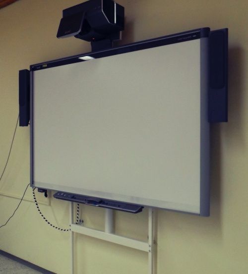 Eine Whiteboard ist an einer Wand montiert, mit einem Lautsprecher oben und zwei zusätzlichen Lautsprechern an den Seiten.