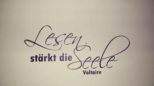 Ein weißer Hintergrund mit einem violetten kursiven Zitat, das 'Lesen stärkt die Seele' von Voltaire besagt.