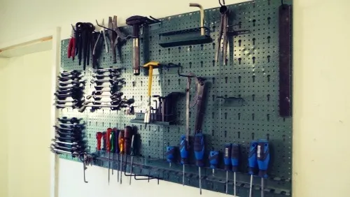 Eine grüne Pegboard-Wand mit verschiedenen Werkzeugen wie Hämmern, Schraubenschlüsseln, Schraubendrehern und Zangen ordentlich aufgehängt und an der Wand befestigt.