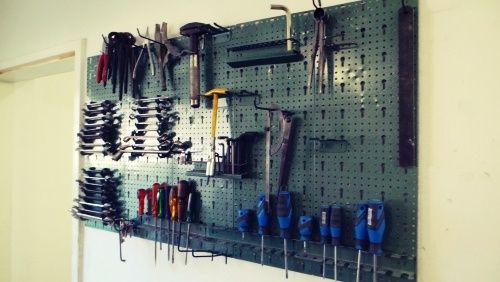 Eine grüne Pegboard-Wand mit verschiedenen Werkzeugen wie Hämmern, Schraubenschlüsseln, Schraubendrehern und Zangen ordentlich aufgehängt und an der Wand befestigt.