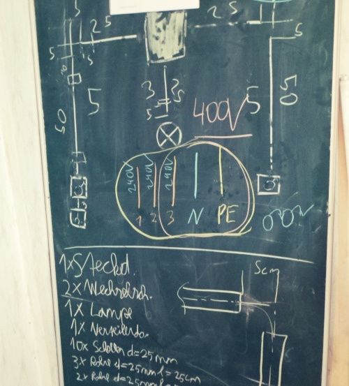 Eine Tafel zeigt handgeschriebene Diagramme und Text. Es enthält Zahlen, Symbole und Gleichungen, die sich auf elektrische Schaltkreise beziehen. Der Text listet Komponenten wie '1x Steched', '2x Wechselrohr' und '1x Lampe' auf.