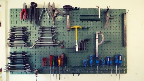 Ein grünes Pegboard zeigt verschiedene Werkzeuge, darunter Hämmer, Schraubenschlüssel und Schraubendreher, ordentlich in Reihen und Spalten angeordnet.