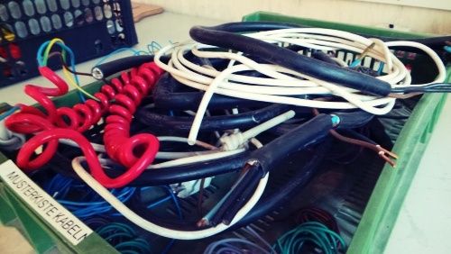 Ein grüner Container gefüllt mit verschiedenen Arten von Kabeln, darunter schwarz, weiß, rot und blau. Ein Aufkleber auf dem Container lautet 'MISTERSTE KABELL'.