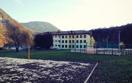 Ein Außensportplatz mit einem gelben Volleyballnetz vor einem großen Gebäude mit Bergen im Hintergrund.