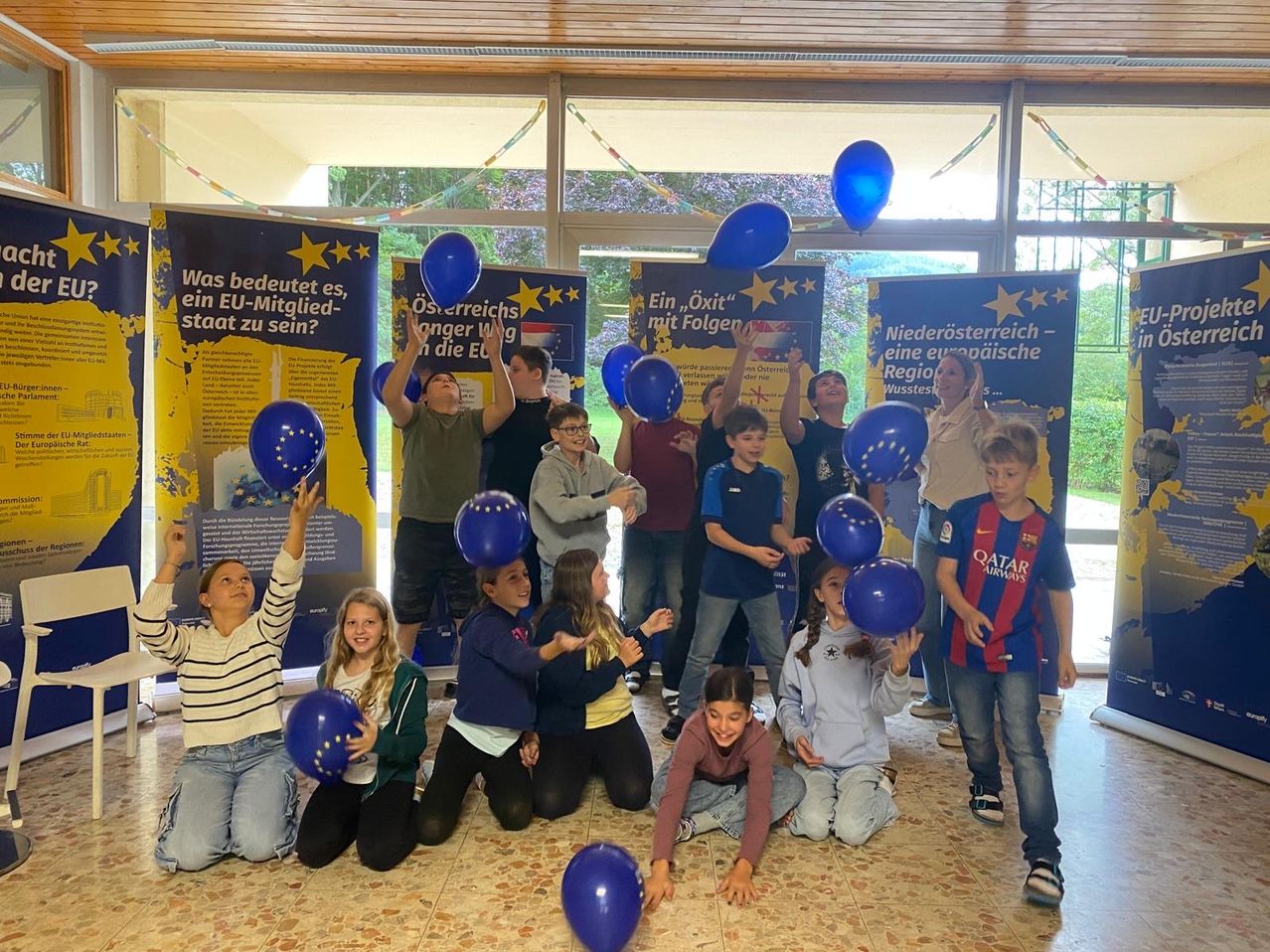 Kinder und Erwachsene halten blaue Luftballons vor Bannern mit Texten über die Europäische Union.