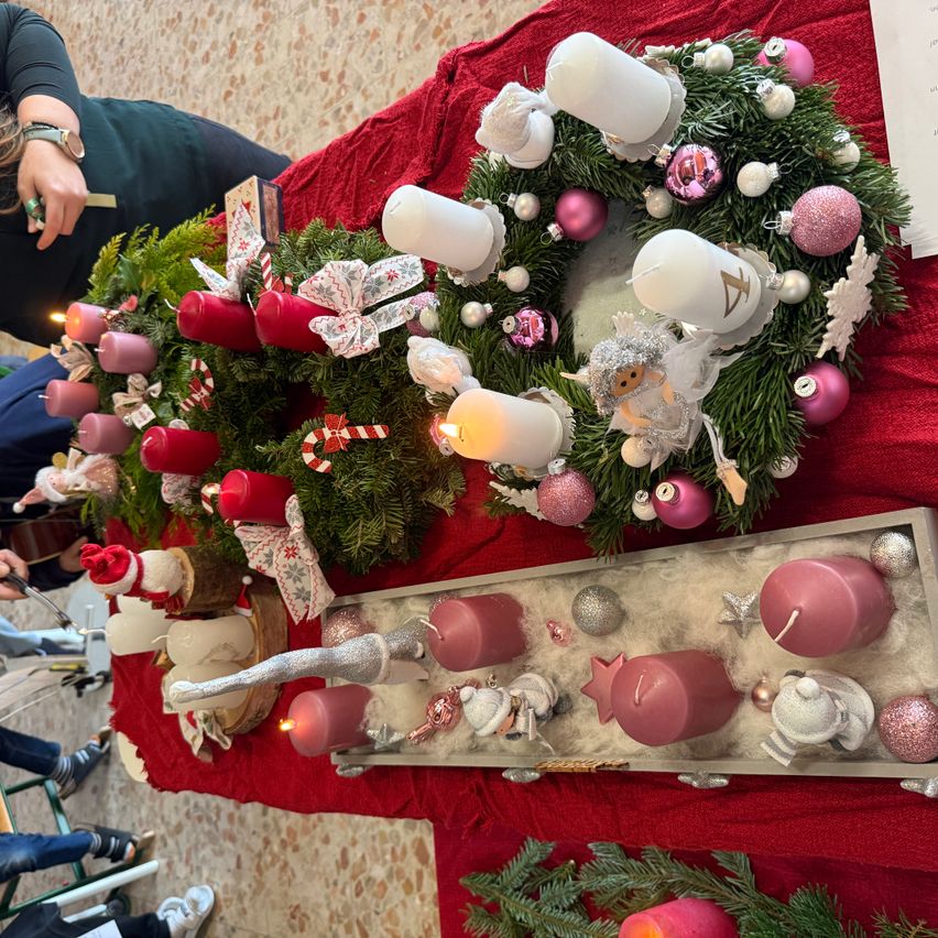 Ein Weihnachtsdisplay mit zwei Kränzen und mehreren Kerzen, ein Kranz hat einen rosa Engel und der andere einen roten Weihnachtsmann, arrangiert auf einem roten Tischtuch.