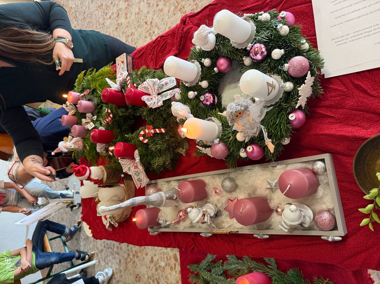 Ein Weihnachtsdisplay mit zwei Kränzen und mehreren Kerzen, ein Kranz hat einen rosa Engel und der andere einen roten Weihnachtsmann, arrangiert auf einem roten Tischtuch.
