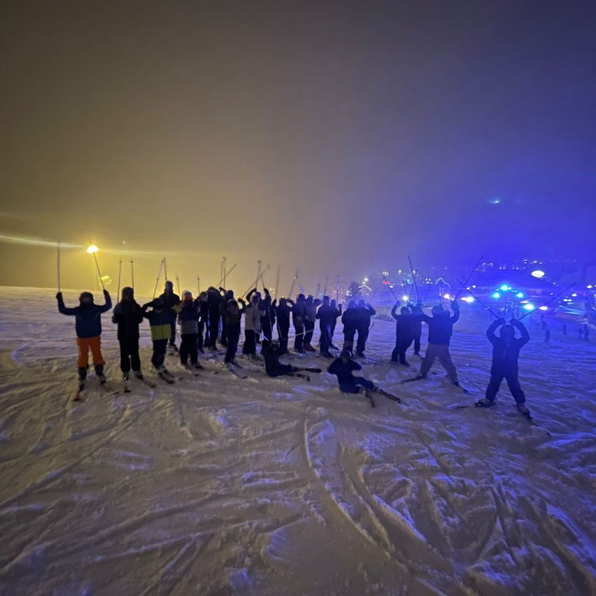 Eine Gruppe von Skifahrern in Winterkleidung posiert für ein Foto im Schnee bei Nacht.