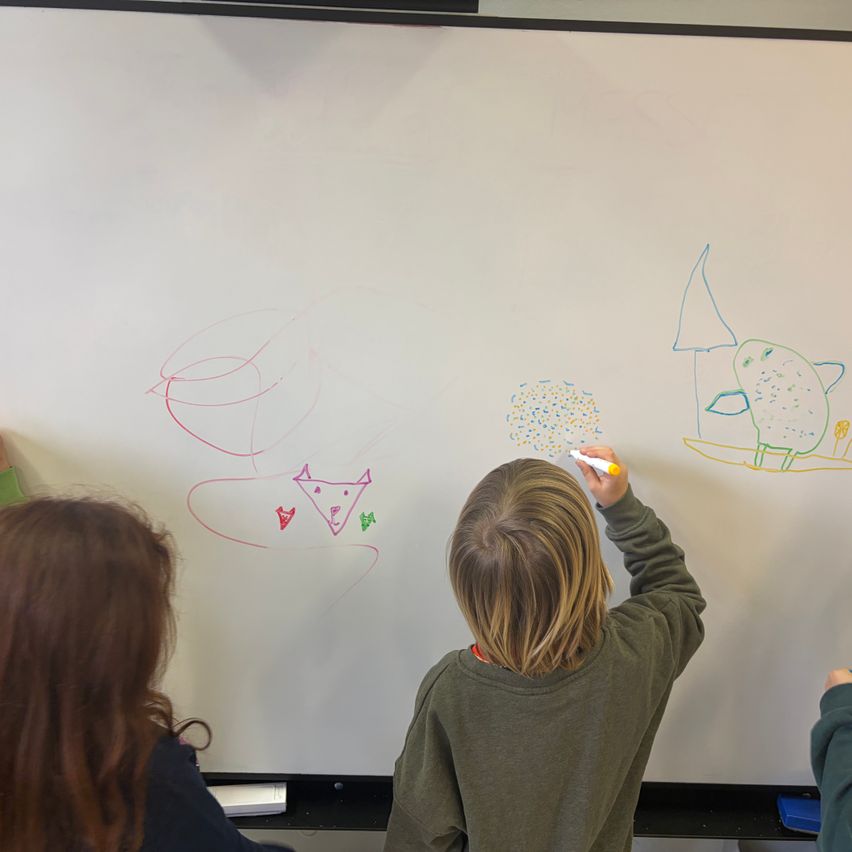 Kinder zeichnen auf einer Tafel mit verschiedenen Zeichnungen und Formen, ein Kind benutzt einen gelben Marker.