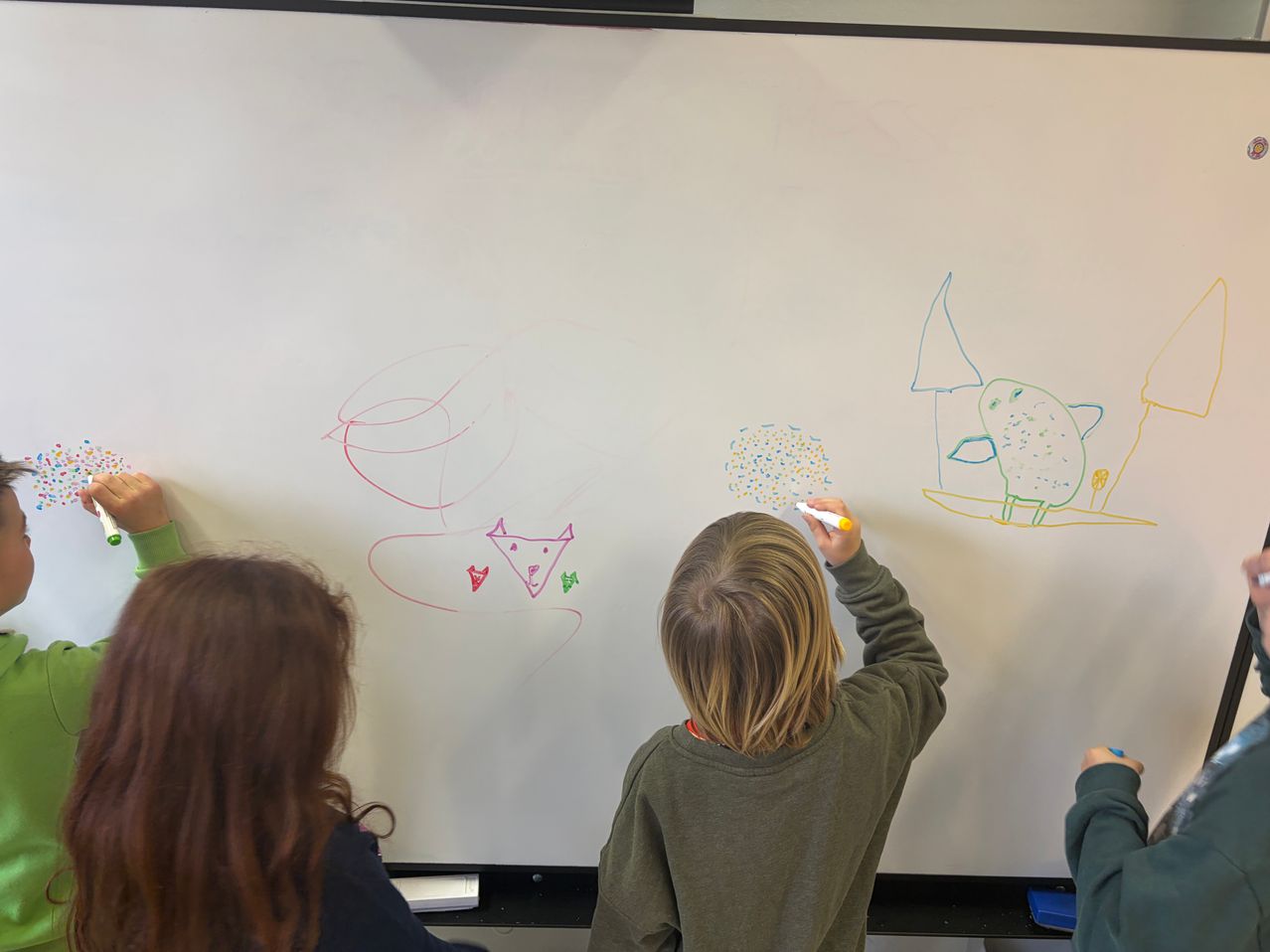 Kinder zeichnen auf einer Tafel mit verschiedenen Zeichnungen und Formen, ein Kind benutzt einen gelben Marker.
