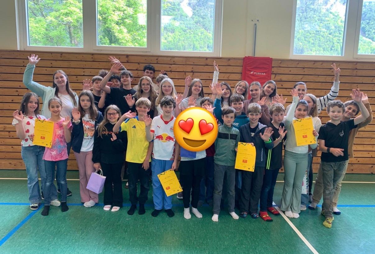 Group photo of students inside a gym with some holding certificates, smiling, and making hand gestures with a heart emoji in the center.