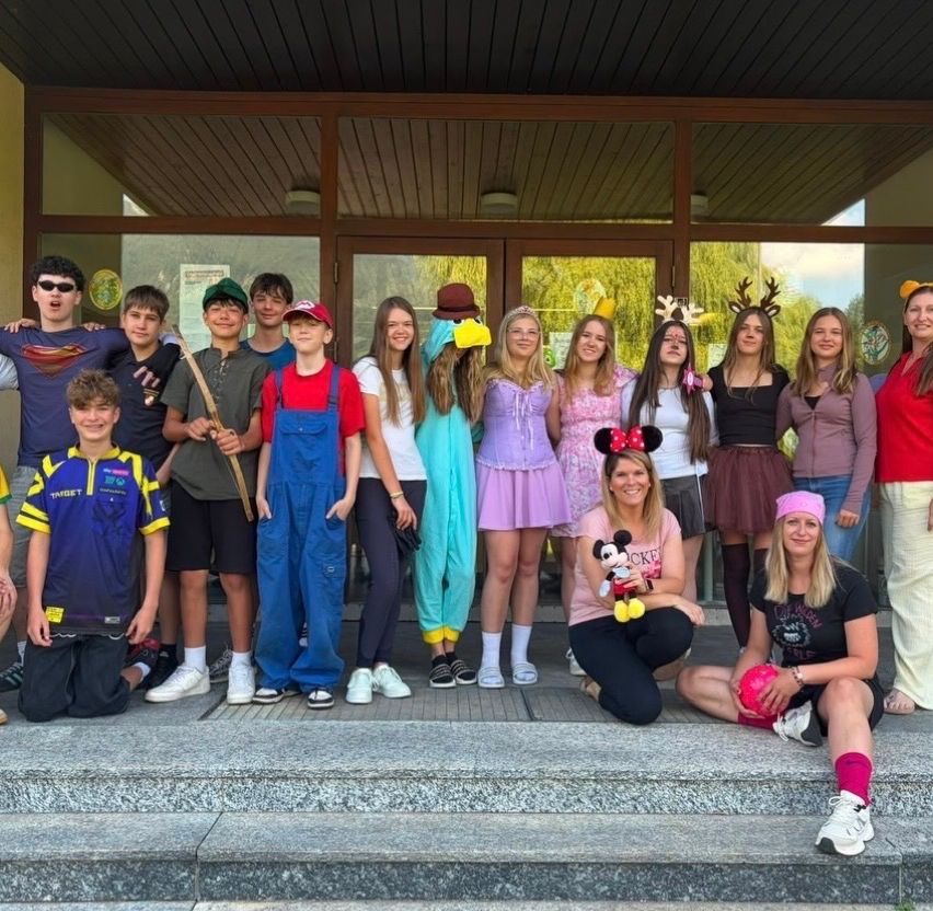 Eine Gruppe junger Menschen und Erwachsener in Kostümen posiert für ein Foto auf den Stufen eines Gebäudes. Die Kostüme reichen von Superhelden bis hin zu Disney-Charakteren.