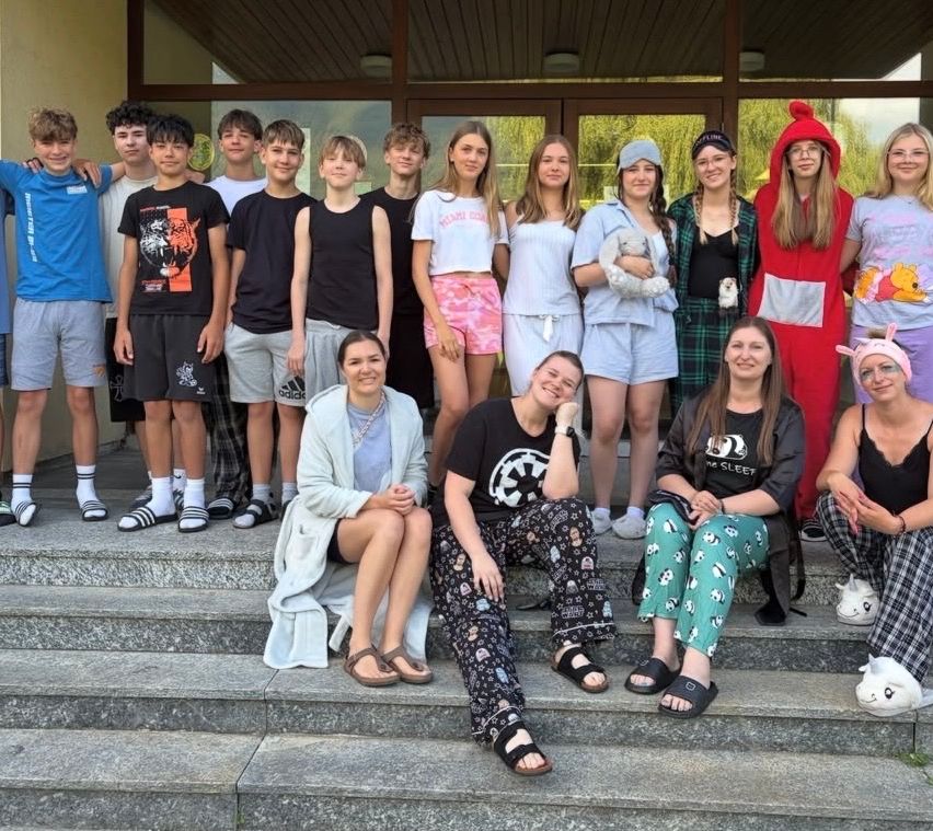 Eine Gruppe junger Menschen und Erwachsene posiert für ein Foto auf den Stufen vor einem Gebäude, einige in lässiger Kleidung, andere in Kostümen.