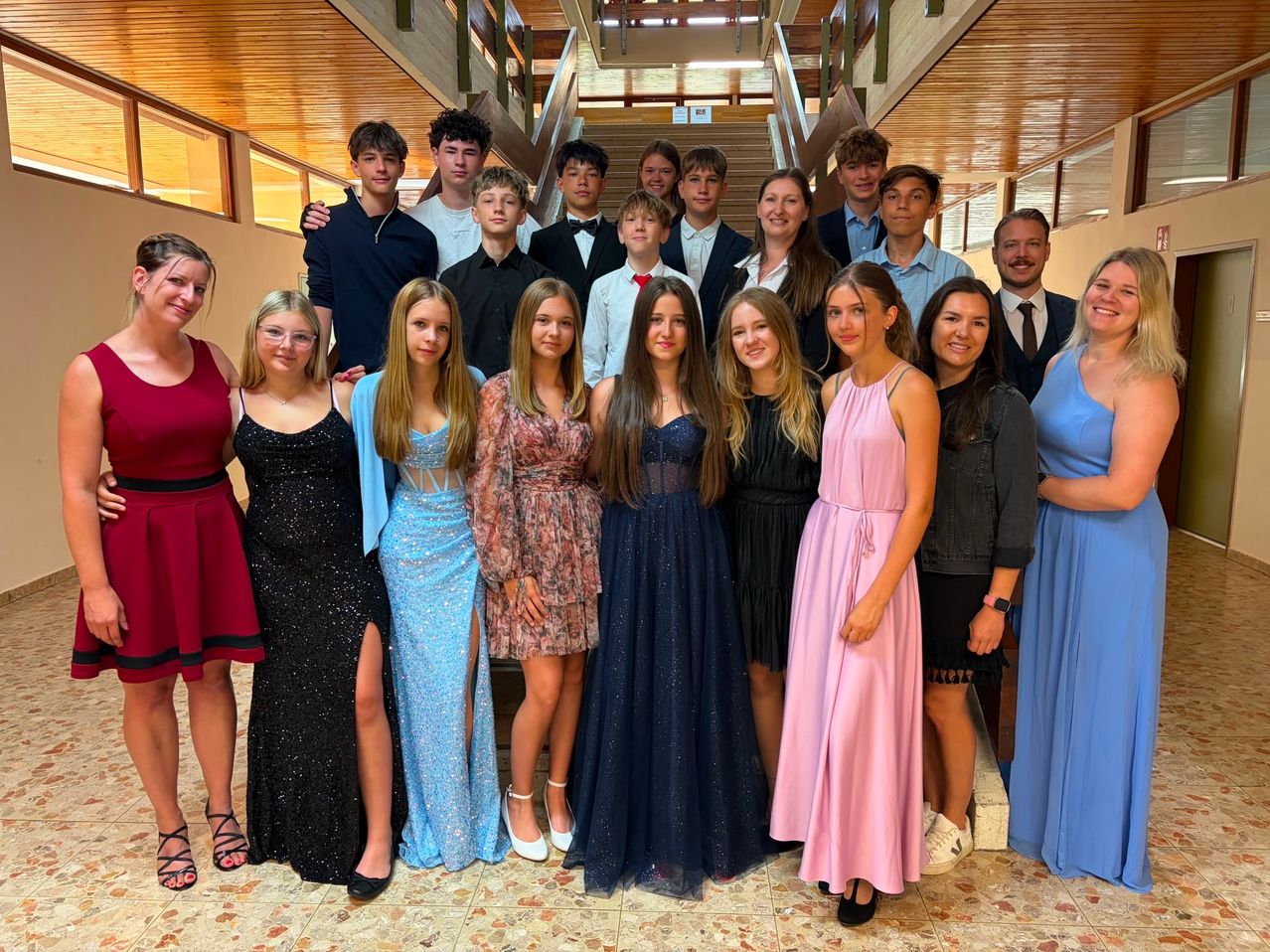 Eine Gruppe junger Erwachsener, sowohl Männer als auch Frauen, posiert für ein Foto in einem Flur. Sie sind in formeller Kleidung gekleidet.