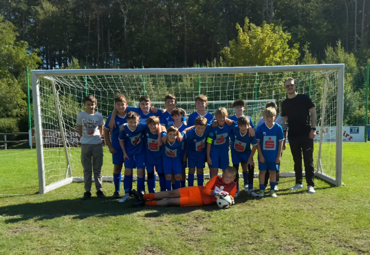 Eine Gruppe junger Fußballspieler in blauen Trikots posiert für ein Foto vor einem Fußballtor.