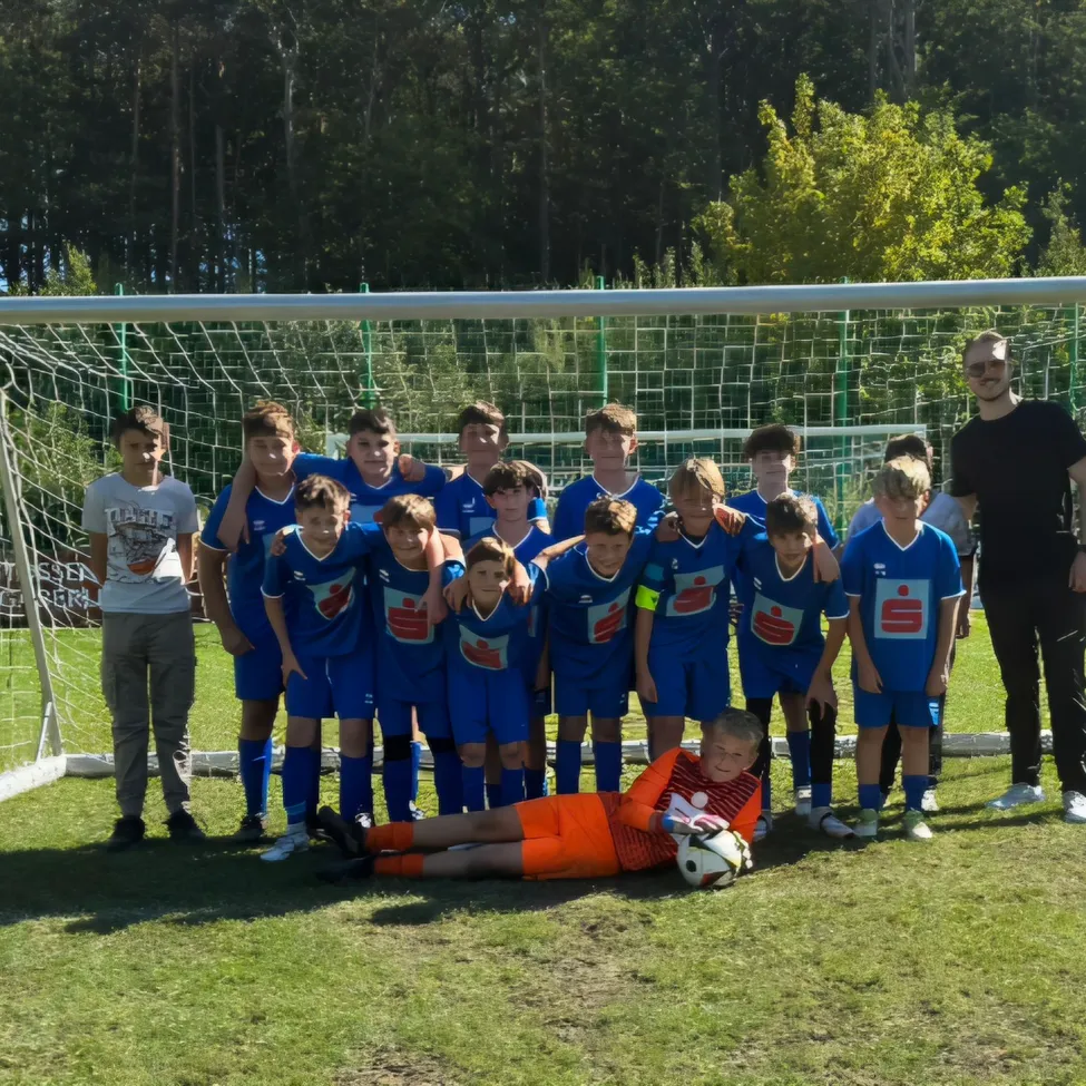 Eine Gruppe junger Fußballspieler in blauen Trikots posiert für ein Foto vor einem Fußballtor.