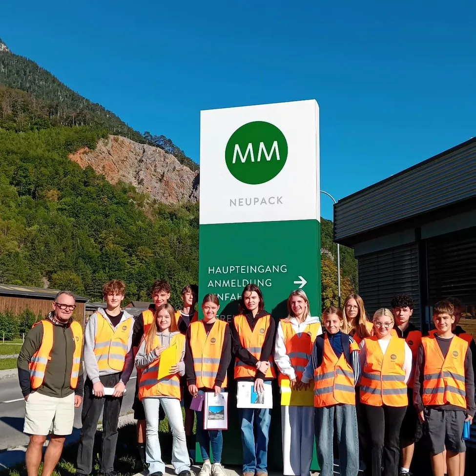 Eine Gruppe von Menschen in Sicherheitswesten posiert für ein Foto vor einem Schild, das 'Neupack' sagt.