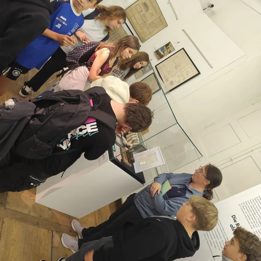 Eine Gruppe von Kindern und Erwachsenen versammelt sich um eine Glasvitrine in einem Museum.
