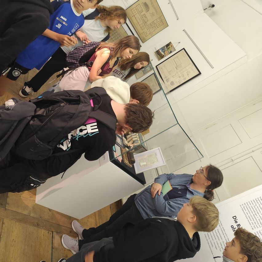 Eine Gruppe von Kindern und Erwachsenen versammelt sich um eine Glasvitrine in einem Museum.