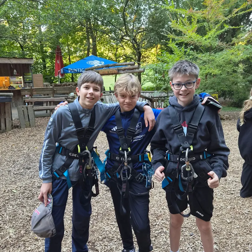Drei junge Jungen in Gurten stehen zusammen im Wald. Sie lächeln und posieren für ein Foto.