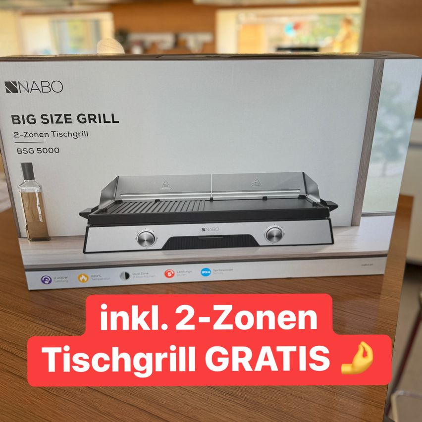 Die Box eines Naboo Big Size Grills steht auf einem Holztisch, inklusive eines kostenlosen Tischgrills. Der Grill hat zwei Zonen und einen 2-Zonen-Tischgrill.